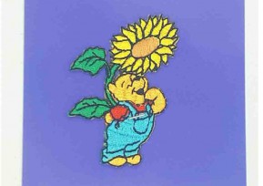 Een Winnie the Pooh applicatie,  met een afmeting van  6 x 4.5 cm.   Opstrijkbaar. Winnie staand onder de zonnebloem.           